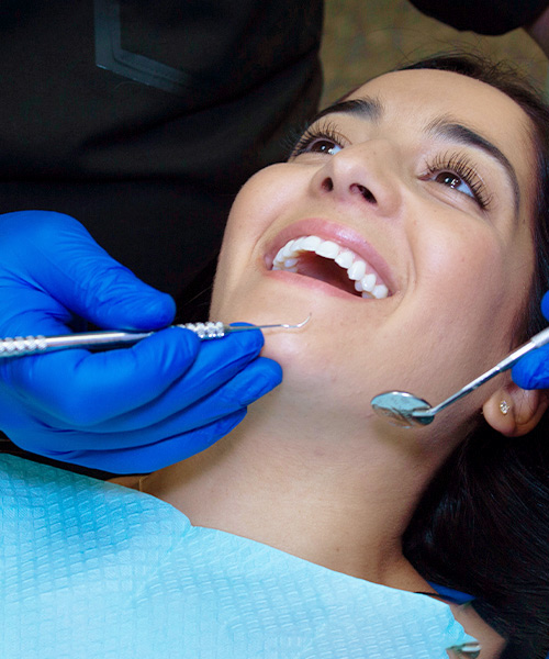 Hygienist with Patient Dental exams and cleanings, available through our dental practice in West Bloomfield, Michigan, are essential to your oral health. In this image, a woman smiles as a hygienist cleans her teeth.