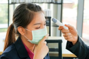 A patient who is wearing a mask has her temperature taken. When we reopen our dental office, we will take several additional safety precautions.