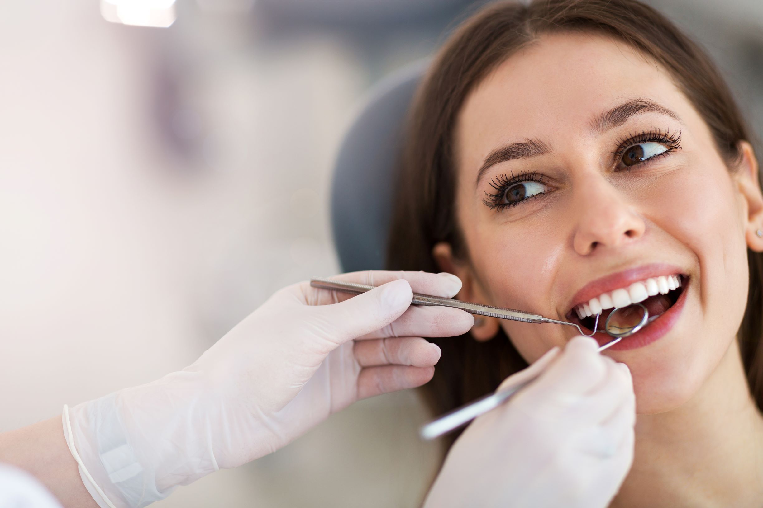 The Fienman Dental PLLC Membership Plan offers numerous money-saving benefits for patients who do not have dental insurance. This image shows a woman smiling as a dental professional uses a mirror to see the back of her teeth.