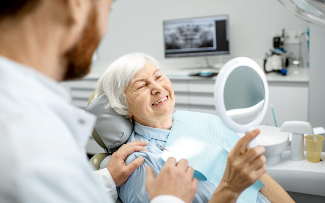 There are many differences in deep cleaning vs. regular dental cleaning. In this image, a woman smiles as she looks at her teeth in a handheld mirror in a dentist's chair.