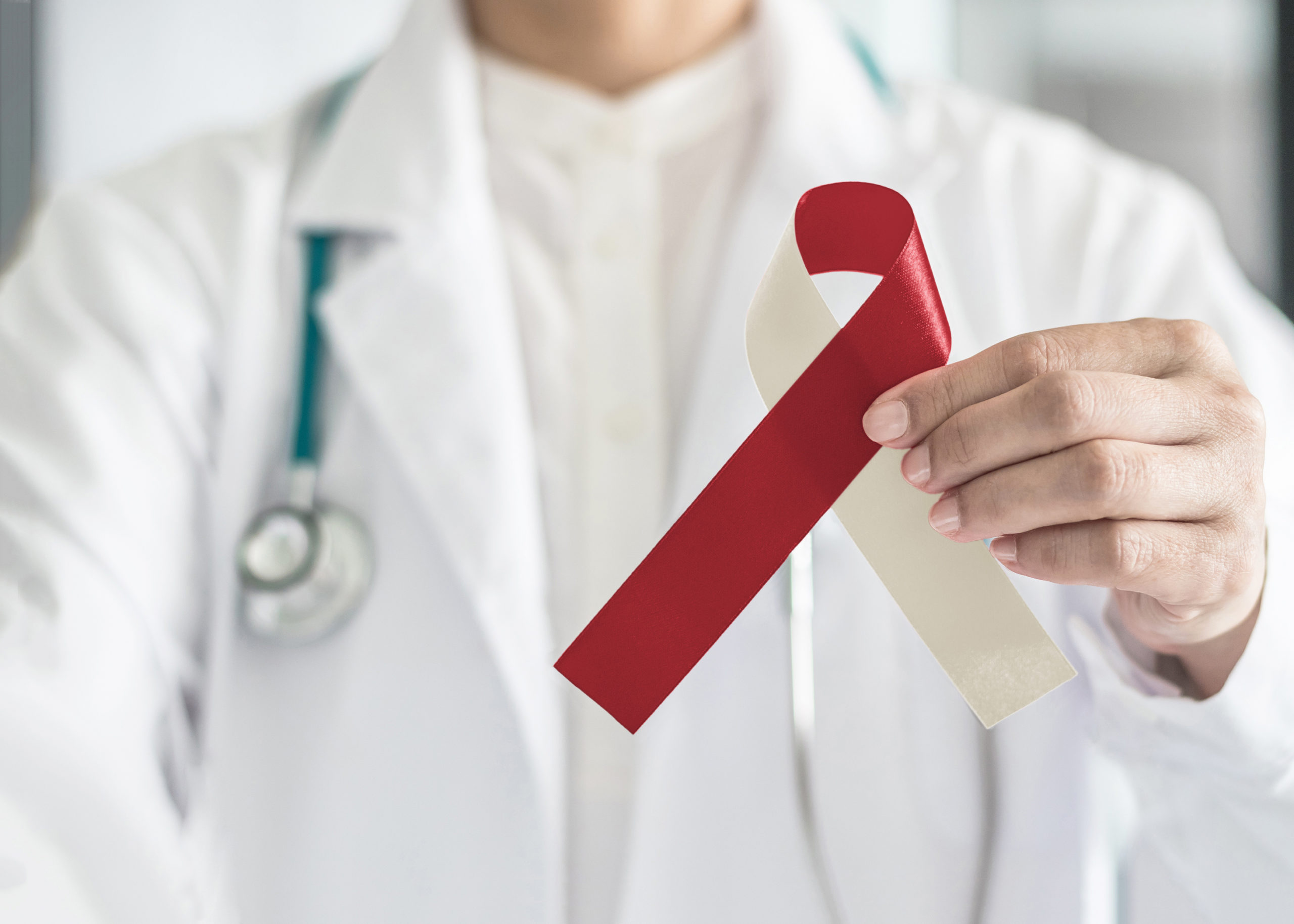 The dentist looks for signs of oral cancer during a regular checkup. This is a closeup image of a burgundy and ivory ribbon held by a doctor. The ribbon represents head and neck cancer, oral squamous cell carcinoma, throat, laryngeal and pharyngeal cancer awareness.