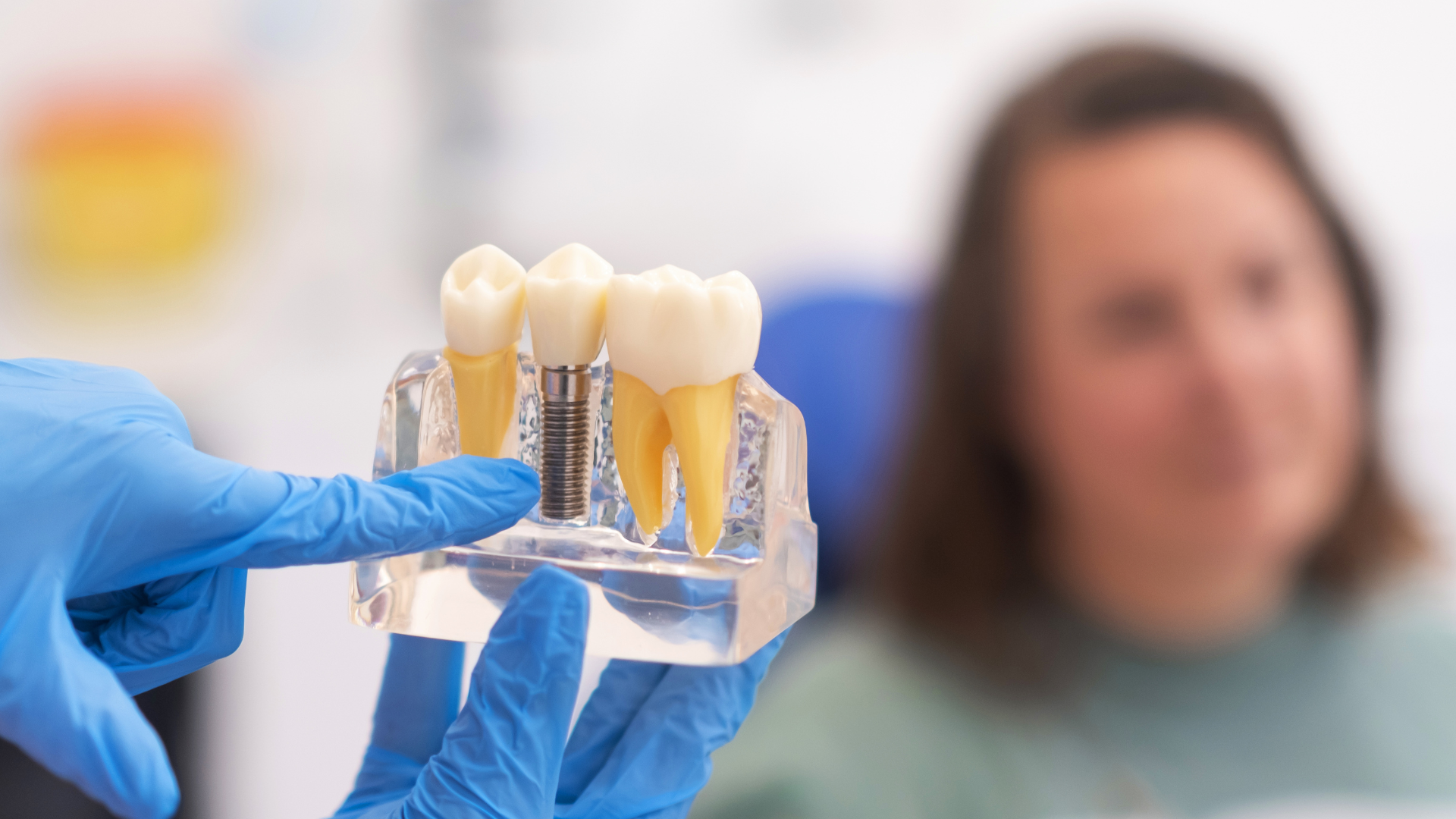 Dentist pointing at an example of a dental implant crown close-up to discuss maintenance with a patient from a west Bloomfield dentistry