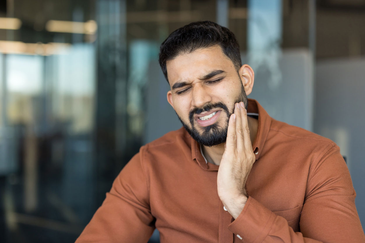 Adult holding their cheek from tooth pain before a same-day emergency dental visit